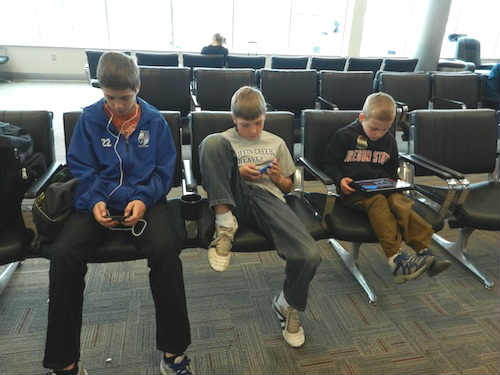 kids at the airport departure area playing gadgets