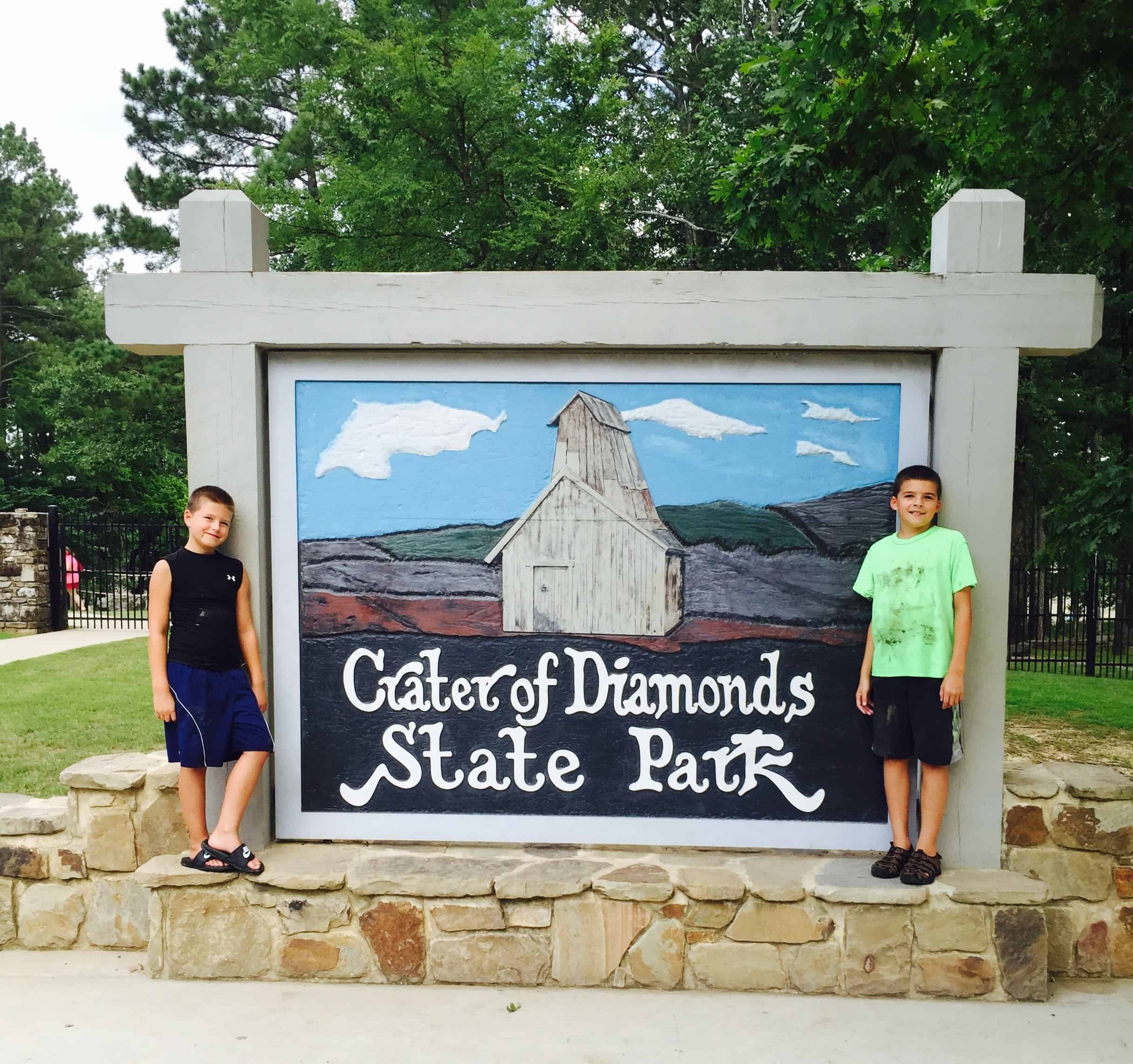 2 boys standing both sides of Crater of Diamonds State Park sign