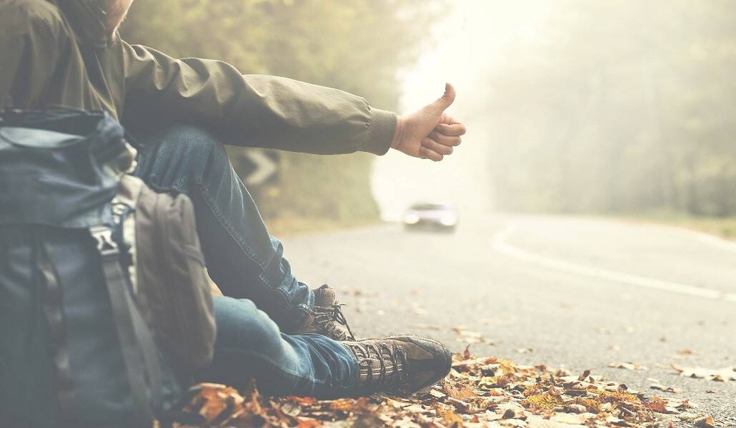 man sitting on the side of road hitchhiking